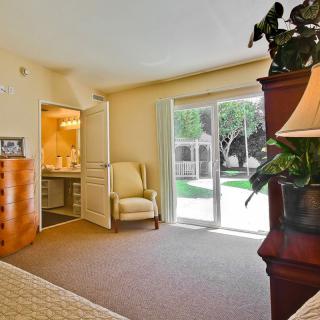 A cozy bedroom with natural light streaming through a sliding door, featuring an armchair and warm decor.