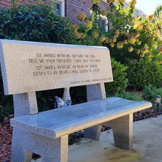 A beautifully crafted stone bench featuring an inscription, set in a serene outdoor environment.