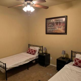 A simple bedroom with two twin beds, a painting on the wall, nightstands beside each bed, and a ceiling fan overhead.