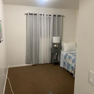 A minimalist bedroom with a single bed, bedside lamp, and light gray curtains.