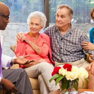A healthcare professional engages in a supportive conversation with an elderly couple and a family member, highlighting the importance of care and communication.
