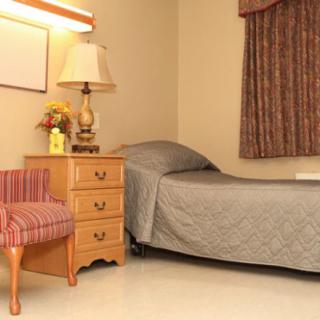 A simple bedroom with a single bed, nightstand, lamp, and chair.