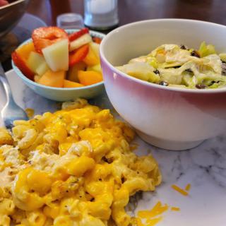 A delicious meal with mac and cheese, fruit salad, and a bowl of avocado salad.