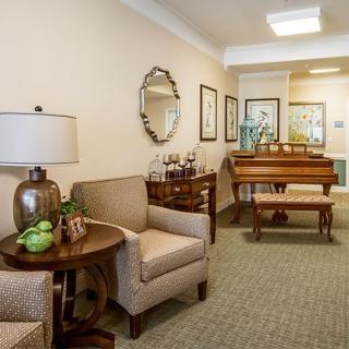 A cozy living room featuring a piano, armchairs, and elegant decor with neutral tones.