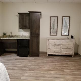 A modern interior featuring a kitchenette with dark cabinetry and a light-colored dresser on hardwood flooring.