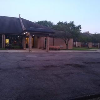 A quiet evening view of a building with a canopy and surrounding trees, captured from a parking lot.
