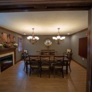A cozy dining room with a large table, chairs, a chandelier, and a fireplace.