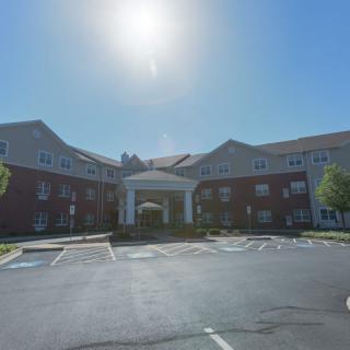 A sunny day view of a large building with a parking lot in front.
