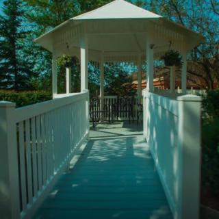 A scenic view of a white gazebo with a wooden walkway surrounded by greenery.