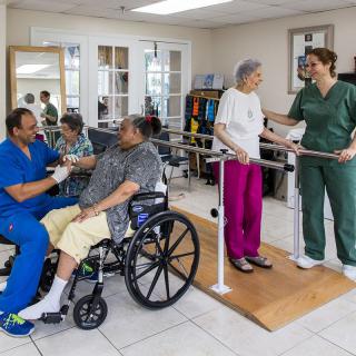 Elderly patients receiving physical therapy in a rehabilitation facility with assistance from healthcare professionals.