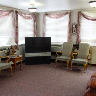A traditionally styled living room with a large television, ornate chairs, and decorative curtains.