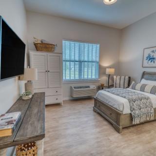 A cozy and well-decorated bedroom featuring a comfortable bed, a large television, a dresser, and bedside lamps.