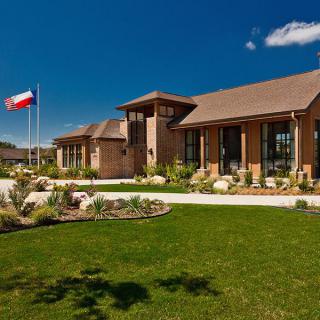 A modern building with a landscaped lawn and a flag under a clear blue sky.
