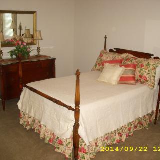 A cozy bedroom with a wooden bed and dresser, featuring floral bedding and decorative cushions.