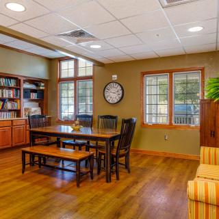 A cozy office interior with a wooden table, chairs, and a bookshelf.