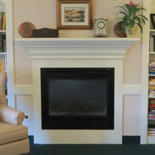 A cozy living room featuring a stylish fireplace with a decorated mantel, adjacent to a bookshelf and comfortable chair.