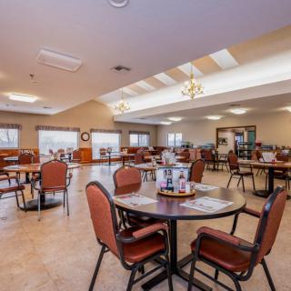 A spacious dining area with neatly arranged tables and chairs, featuring large windows and overhead lighting.