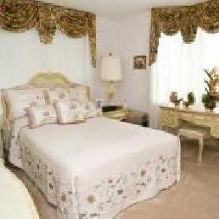 A traditional bedroom with neutral colors and elegant decor, featuring a bed, decorative pillows, and classic furnishings.
