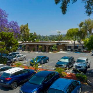 A parking lot filled with cars surrounded by trees and a building in the background.