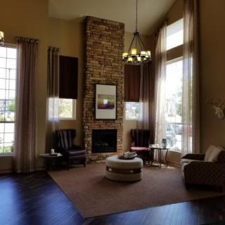 A spacious living room featuring a stone fireplace, large windows with curtains, and a cozy seating area with armchairs and a coffee table.