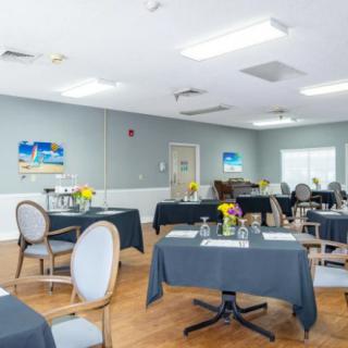 A well-lit dining area with neatly arranged tables and chairs, decorated with flowers and paintings on the walls.