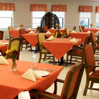 A well-decorated dining room with orange tablecloths and floral centerpieces, ready for guests.