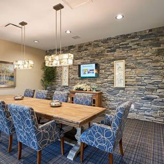 A modern dining or conference room featuring a stone accent wall, a large wooden table surrounded by upholstered chairs, and elegant lighting fixtures.