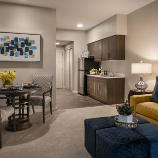 A modern living room with a dining area and kitchenette, featuring stylish furniture and abstract artwork.