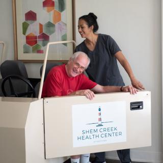 A healthcare professional assists an elderly patient with rehabilitation exercises at a health center.