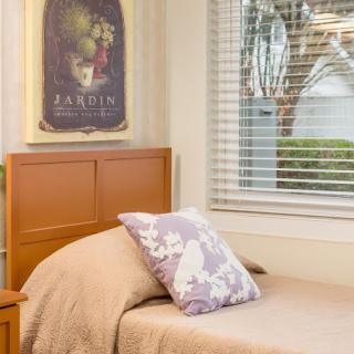 A cozy single bedroom with a pillow on the bed, a poster on the wall, and a window allowing daylight in.