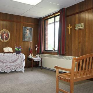 A small chapel room with wooden walls, featuring an altar adorned with religious icons and a cross.