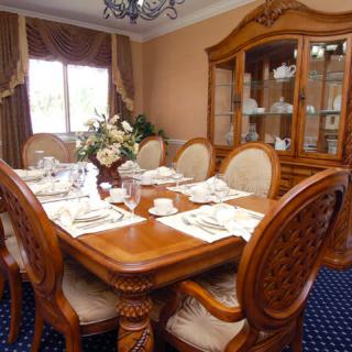 A traditional dining room with a wooden table and chairs, elegantly set for a meal, featuring a china cabinet and decorative curtains.