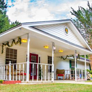 A charming white cottage with a welcoming porch surrounded by lush greenery.