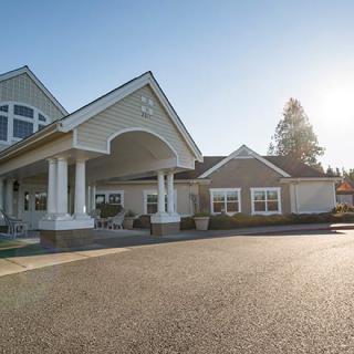 A large, modern residential building with a covered entrance and a spacious driveway under clear skies.