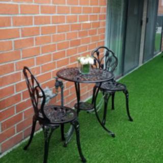 A cozy outdoor patio setup with a small table and two chairs on artificial grass.