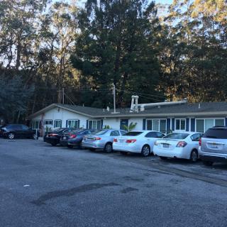A quaint motel surrounded by trees, featuring a parking area filled with various cars.