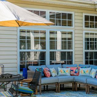 A cozy outdoor patio area with a cushioned sectional sofa and colorful pillows, shaded by an umbrella.