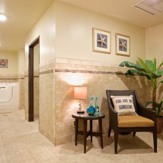 A well-decorated lobby area featuring a chair, a side table with a lamp and decorative items, and framed artwork on the wall.