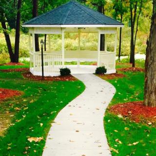 A scenic garden pathway leads to a charming white gazebo surrounded by lush greenery.