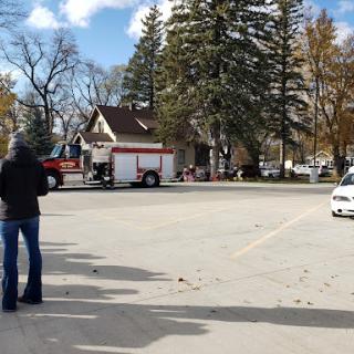 A view of a parking lot featuring a fire truck with trees showcasing autumn colors in the background.