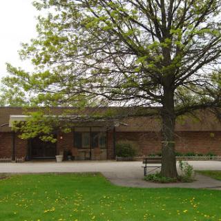 A serene outdoor space featuring a brick building, a large tree, and green grass.