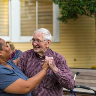 An elderly couple joyfully dancing together outside.