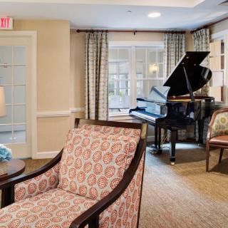 A well-furnished living room featuring a grand piano and upholstered chairs.