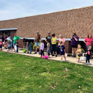 A group of children and adults lined up outside, enjoying a sunny day.