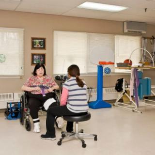 A patient in a wheelchair converses with a therapist in a rehabilitation clinic.