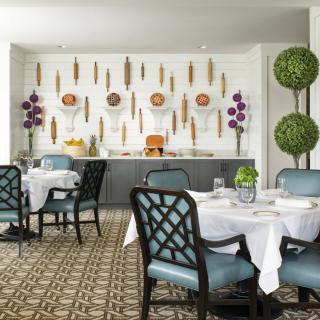 A beautifully designed restaurant dining room featuring elegant tables and chairs, with artistic wall decor and lush greenery.
