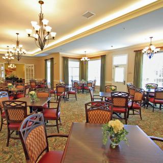 A spacious dining room with elegant decor, featuring multiple tables and chairs under ornate chandeliers.