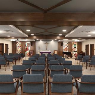 A chapel interior featuring rows of wooden chairs, stained glass windows, and an altar at the front.