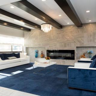 A modern living room with a blue carpet, stylish furniture, beamed ceiling, and a large fireplace.