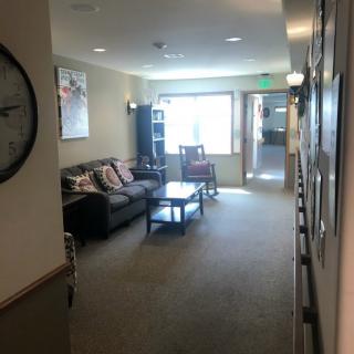A cozy lobby hallway with a sofa, rocking chair, coffee table, and decorative wall clock.